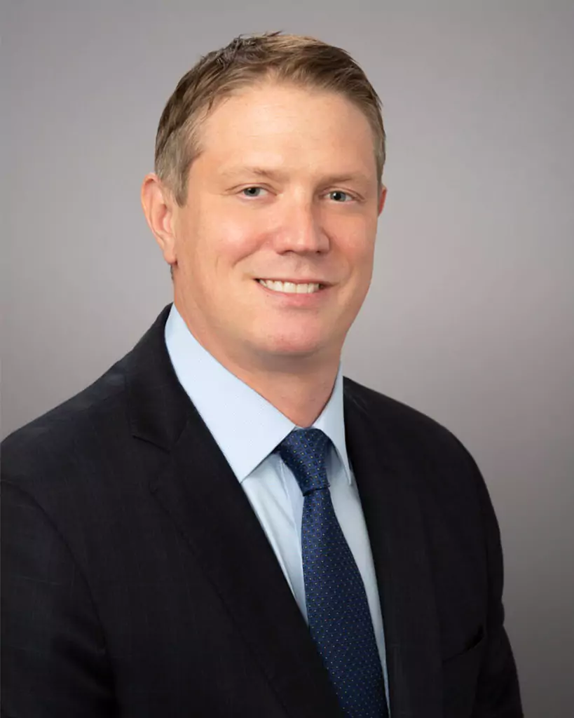 Man in suit smiling against gray background.