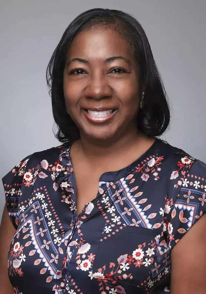 Smiling woman wearing a patterned blouse against a plain backdrop.