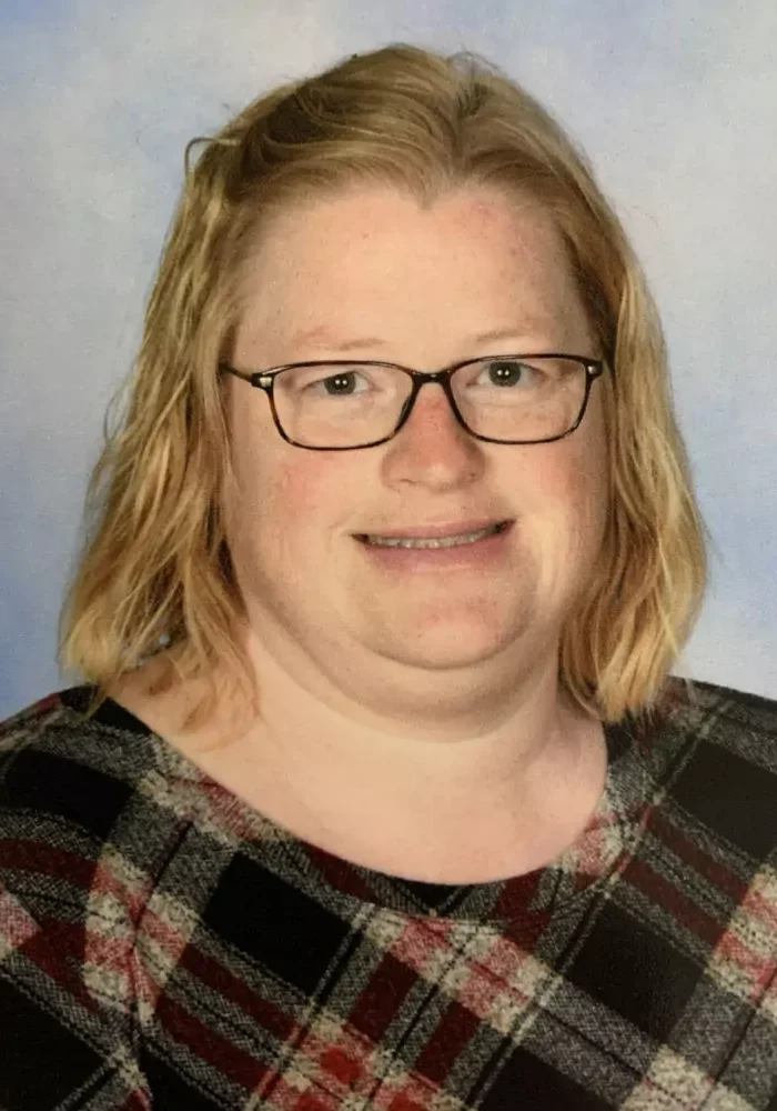 Smiling woman with glasses and blonde hair in plaid shirt.
